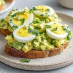 Zesty Avocado Egg Salad on toasted bread topped with sliced hard-boiled eggs and fresh parsley