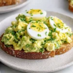 Zesty Avocado Egg Salad served on toasted bread with sliced boiled eggs and fresh herbs
