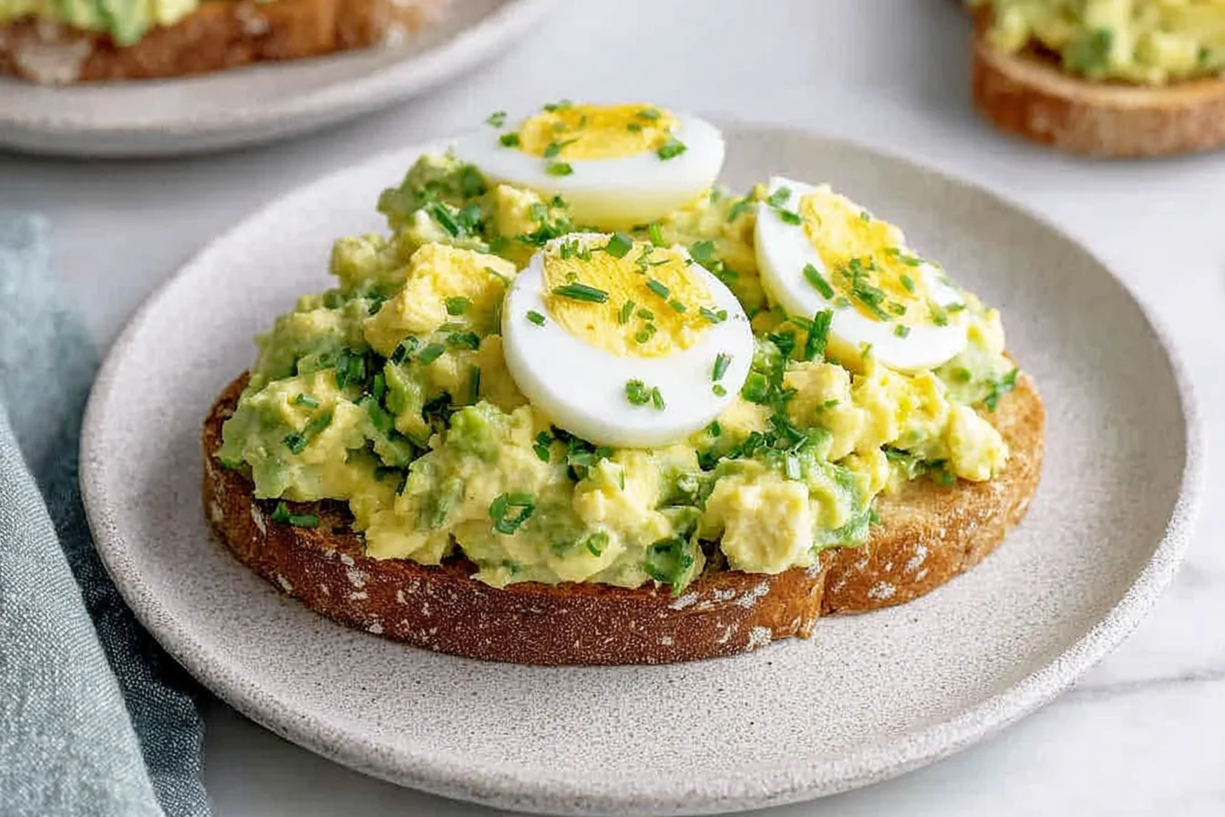 Zesty Avocado Egg Salad served on toasted bread with sliced boiled eggs and fresh herbs