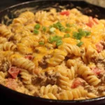 Creamy Rotel Pasta with Ground Beef in a skillet topped with melted cheese and green onions