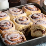 Sourdough Discard Cinnamon Rolls in baking pan with one roll pulled apart showing soft texture