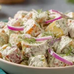 Close-up of Jamaican Potato Salad with creamy vegan dressing, sweet potatoes, red onion slices, and fresh herbs
