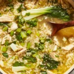 Ginger Chicken and Rice Soup Recipe simmering in a large pot with shredded chicken, bok choy, jasmine rice, and green onions