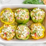 Greek Chicken Stuffed Peppers baked with feta, olives, herbs, and rice in a casserole dish, topped with fresh dill and lemon