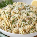 Creamy Lemon Parmesan Pasta Salad topped with shredded Parmesan and fresh parsley beside sliced lemons