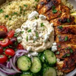 Mediterranean Chicken Bowl with sliced chicken, quinoa, cucumbers, tomatoes, hummus, and feta topping