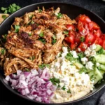 Slow Cooker Chicken Shawarma served in a bowl with hummus, cucumbers, tomatoes, red onion, feta, and naan bread