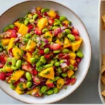 Colorful Mango Strawberry Avocado Edamame Salsa in a bowl with tortilla chips, featuring fresh mango chunks, strawberries, edamame, and herbs