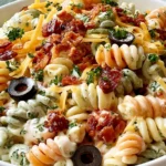 Bacon Ranch Pasta Salad with tri-color rotini, crispy bacon, cheddar cheese, tomatoes, black olives, and creamy ranch dressing