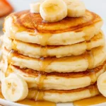 Best Fluffy Pancakes Recipe stacked high with maple syrup and fresh banana slices