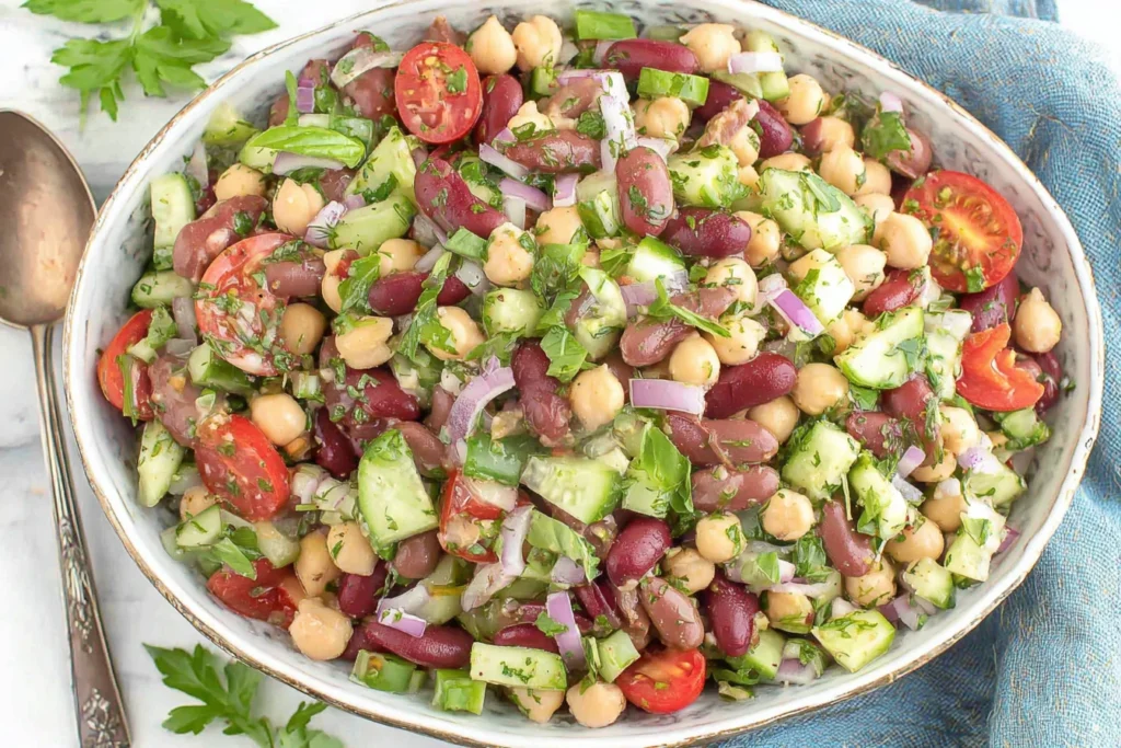 Easy Fresh Mediterranean Bean Salad with chickpeas, kidney beans, cucumber, tomatoes, and fresh herbs in a serving bowl