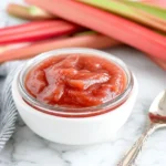 Easy Rhubarb Sauce served in a white bowl with fresh rhubarb stalks in the background