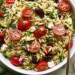 Greek Orzo Pasta Salad served with feta, olives, cucumber, cherry tomatoes, and fresh lemon in a white bowl
