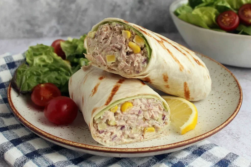 Healthy Tuna Melt Wrap Recipe sliced in half with creamy tuna filling, sweet corn, lemon wedge, and fresh salad on a plate