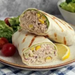 Healthy Tuna Melt Wrap Recipe sliced in half with creamy tuna filling, sweet corn, lemon wedge, and fresh salad on a plate