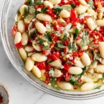 Marinated White Beans in a glass bowl with roasted red peppers, fresh herbs, lemon zest, and olive oil