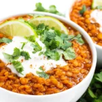 Spicy Mexican Red Lentils Recipe served in a white bowl with sour cream, fresh cilantro, and lime slices