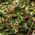 Spring Couscous Salad with peas, arugula, red onions, mint, pistachios, and lemon herb dressing in a serving bowl
