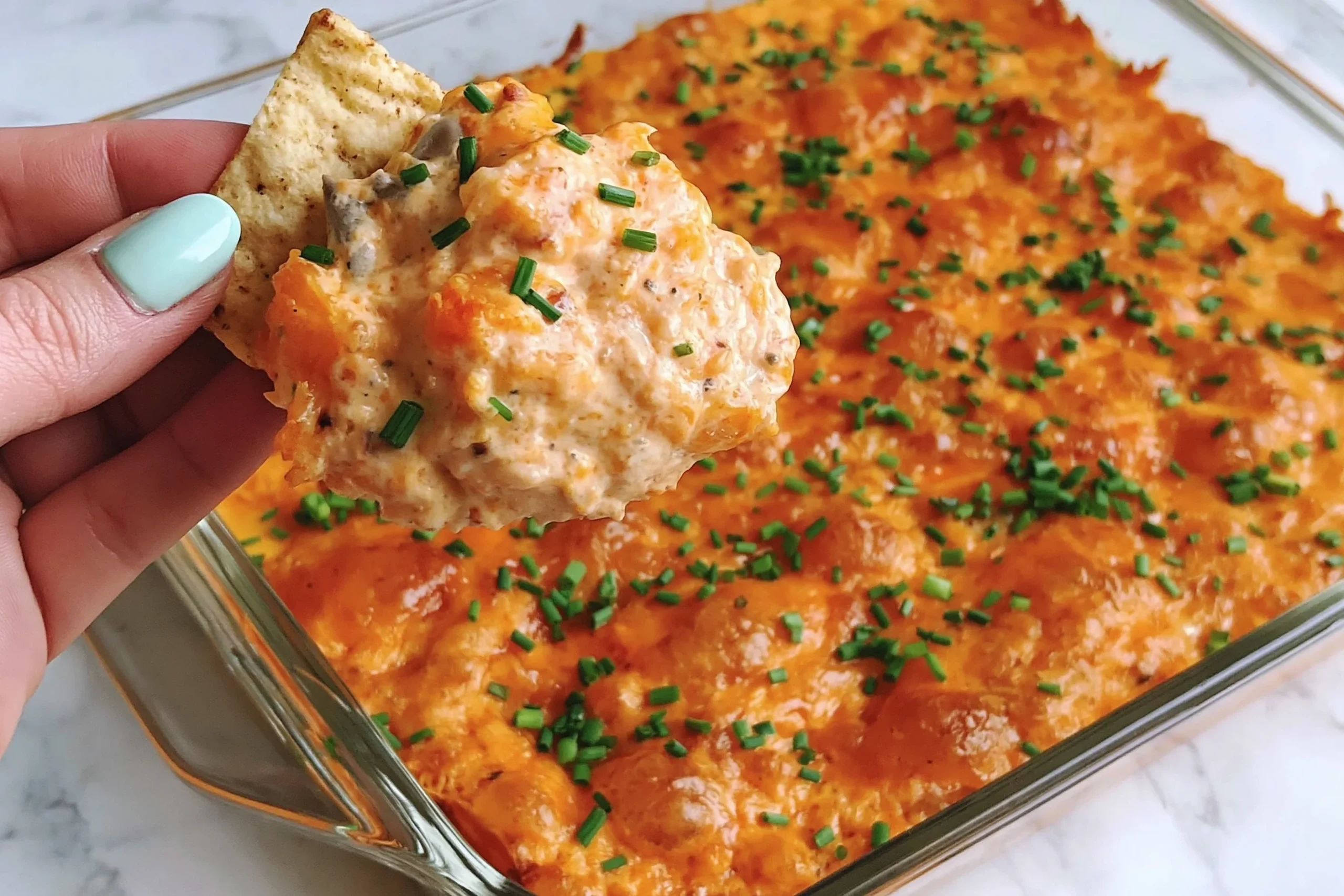 Vegetarian Cheesy White Bean Buffalo Dip served warm with melted cheddar, garnished with chives and scooped with tortilla chips