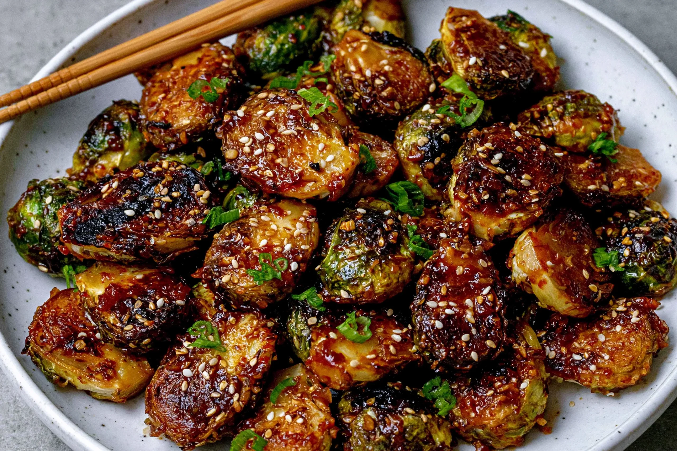 Crispy Asian BBQ Brussels Sprouts coated in a sticky sweet-savory glaze, topped with sesame seeds and green onions