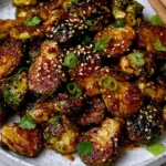 Crispy Asian BBQ Brussels Sprouts glazed in sticky sauce with sesame seeds and sliced green onions on a plate