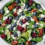 Colorful blueberry spinach salad with honey balsamic dressing, feta cheese, pecans, and fresh berries in a serving bowl