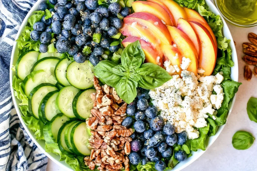 Peach Berry Summer Salad with fresh peaches, blueberries, cucumber, feta, and pecans on a bed of leafy greens