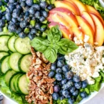 Peach Berry Summer Salad with fresh peaches, blueberries, cucumber, feta, and pecans on a bed of leafy greens