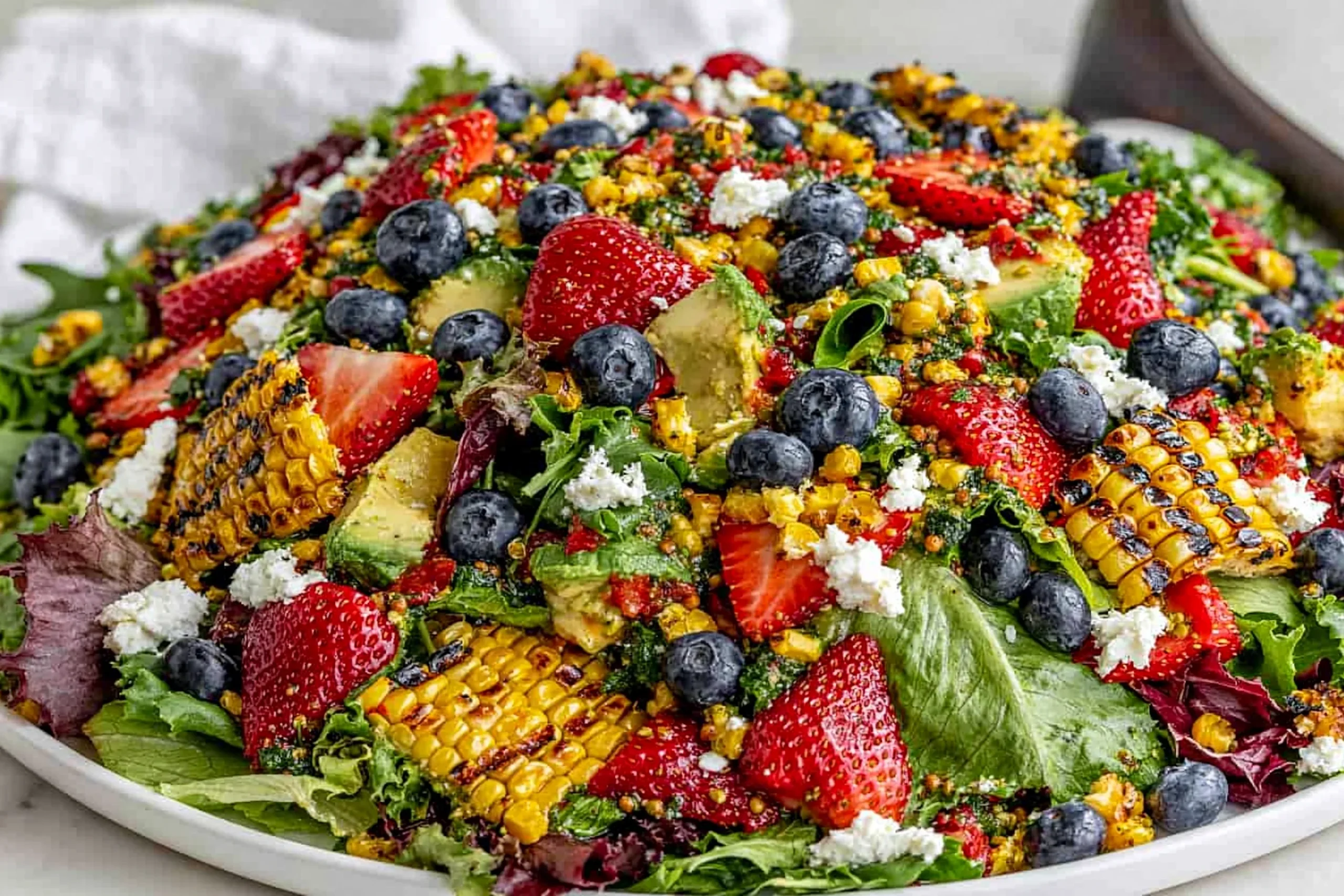 Strawberry Avocado Corn Salad with grilled corn, fresh strawberries, blueberries, avocado, and goat cheese on mixed greens