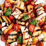 Peach Caprese Salad with grilled peaches, mozzarella chunks, cherry tomatoes, fresh basil, and balsamic glaze close-up