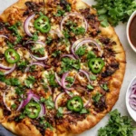 Golden crispy Birria Pizza topped with shredded beef, melted cheese, red onions, jalapeños, and cilantro with consommé on the side