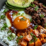 Hot Honey Ground Beef Bowls with rice, avocado slices, roasted sweet potatoes, sesame seeds, and a glossy runny egg with hot honey drizzle