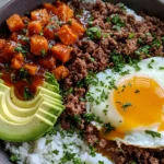 Hot Honey Ground Beef Bowls with roasted sweet potatoes, avocado, rice, and a runny fried egg topped with herbs
