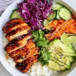 Korean Chicken Rice Bowls with grilled marinated chicken, rice, avocado, cabbage, carrots, and sesame seeds in a vibrant bowl