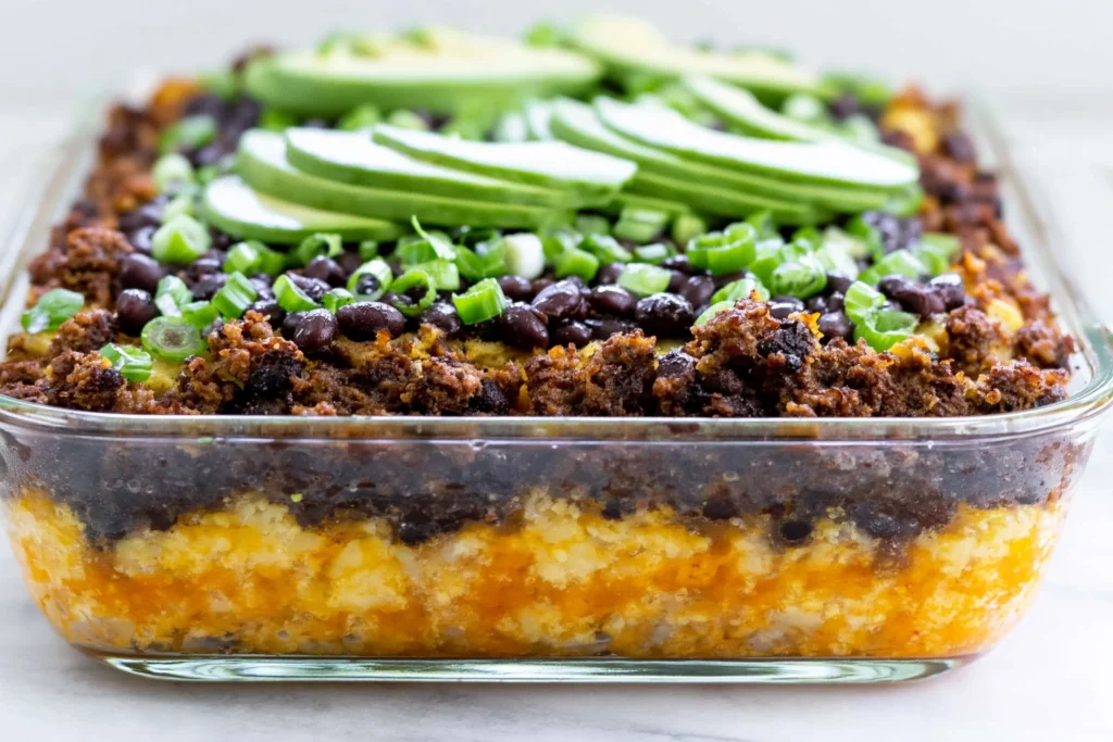 Close-up of Spicy Taco Polenta Bake layered with ground beef, black beans, melted cheese, and topped with avocado slices and green onions