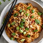 Spicy Peanut Butter Noodles with creamy sauce, chopped peanuts, and green onions in a bowl with chopsticks