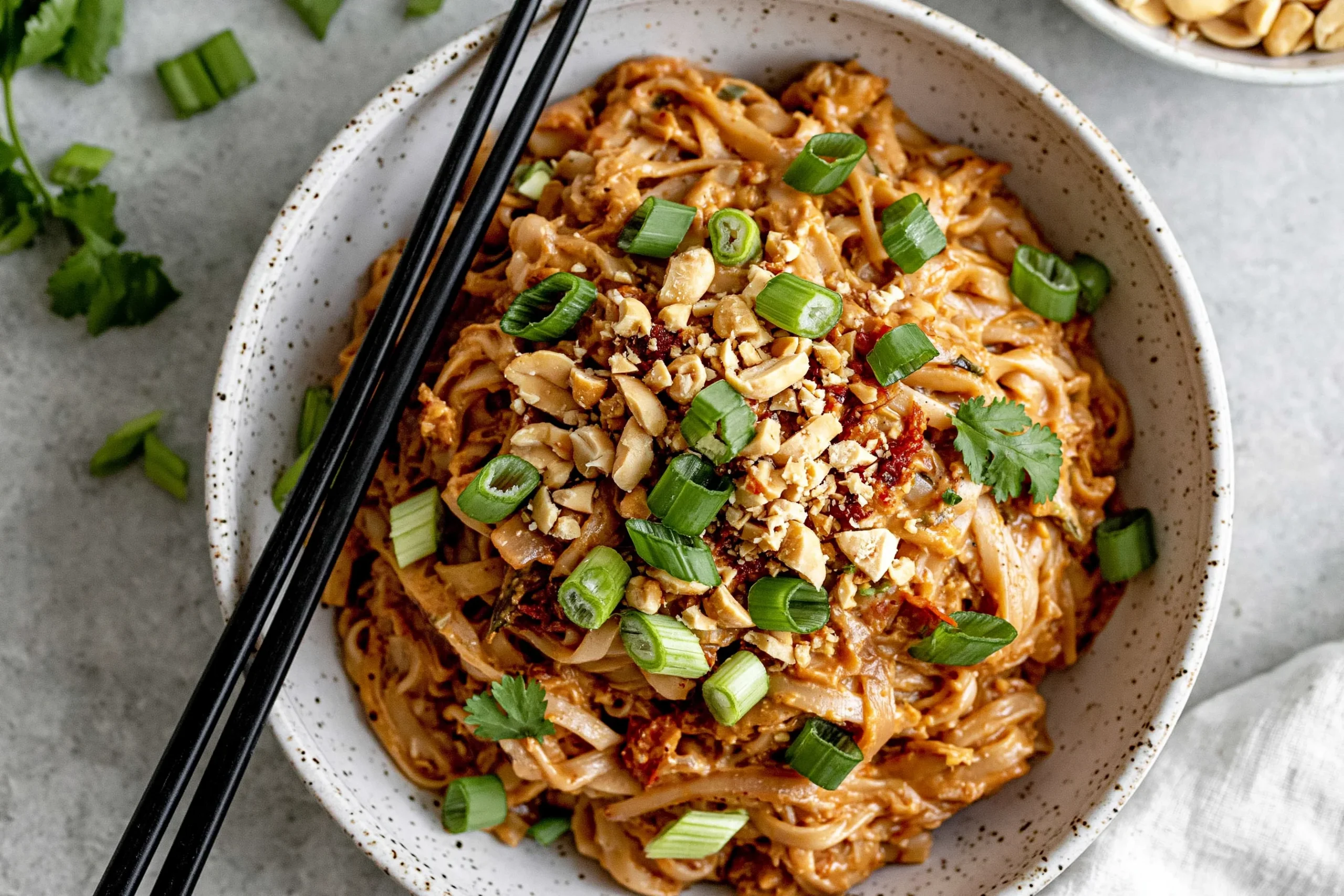 Spicy Peanut Butter Noodles with creamy sauce, chopped peanuts, and green onions in a bowl with chopsticks