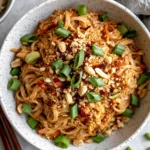 Spicy Peanut Butter Noodles topped with chopped peanuts, green onions, and chili flakes in a rustic bowl
