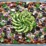 Spicy Taco Polenta Bake topped with avocado, black olives, cilantro, and melted cheese in a casserole dish