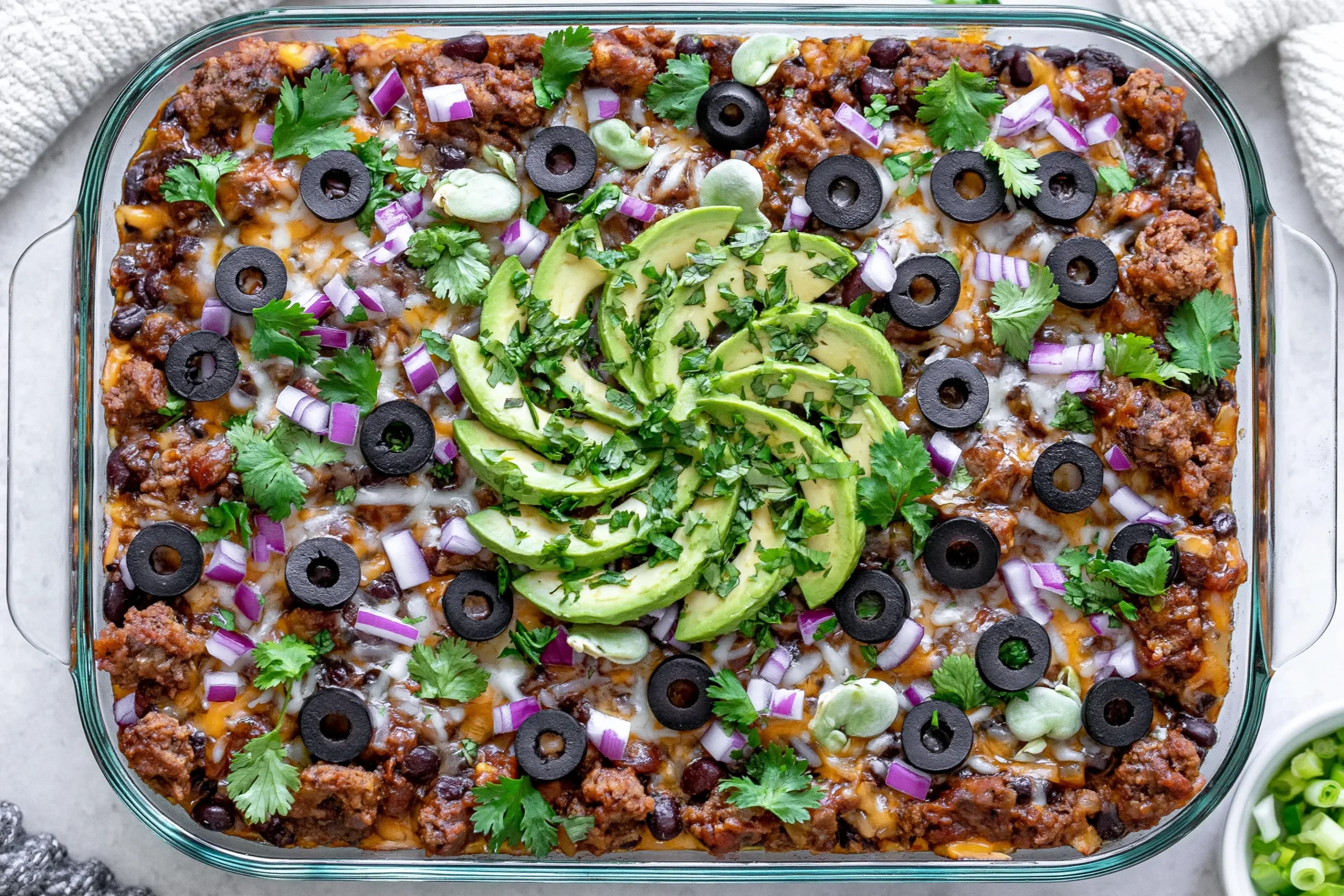 Spicy Taco Polenta Bake topped with avocado, black olives, cilantro, and melted cheese in a casserole dish