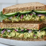 Green Goddess Salad Sandwich with chickpea avocado filling, cucumber, spinach, and whole grain bread stacked on a plate
