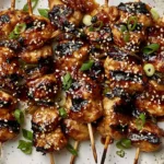Honey Garlic Asian Chicken Kabobs with caramelized glaze, sesame seeds, and green onions on skewers plated for serving
