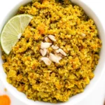 Coconut Curry Quinoa topped with sunflower seeds and a fresh lime wedge in a white bowl.
