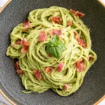 Avocado Carbonara with creamy avocado linguine, crispy bacon pieces, and fresh basil served in a dark ceramic bowl.