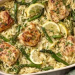 Creamy Orzo with Chicken and Asparagus in a skillet with lemon slices, seared chicken, and fresh herbs