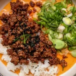 Crispy Ground Beef and Rice with creamy gochujang broth, jasmine rice, green onions, vegetables, and black sesame seeds.