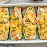 Chicken Stuffed Zucchini Boats with creamy chicken, tomatoes, herbs, and melted cheese baked in a white casserole dish.