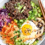 Korean Beef Bowl with ground beef, fried egg, cabbage, carrots, avocado, and spicy sauce over rice