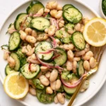 Dilly White Bean Cucumber Salad served on a plate with creamy white beans, crisp cucumbers, red onion, fresh dill, and lemon wedges.