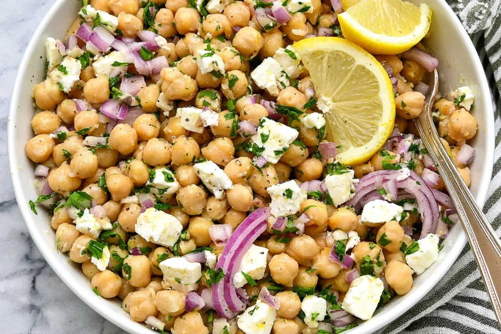 Lemony Chickpea Feta Salad with chickpeas, feta cheese, red onion, parsley, and fresh lemon slices in a bowl